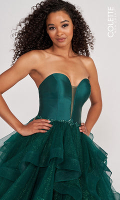 A woman wearing the Colette Glitter-Tulle Layered Long Prom Ball Gown, featuring a strapless fitted bodice and an emerald green glittery tulle skirt, stands against a plain background.