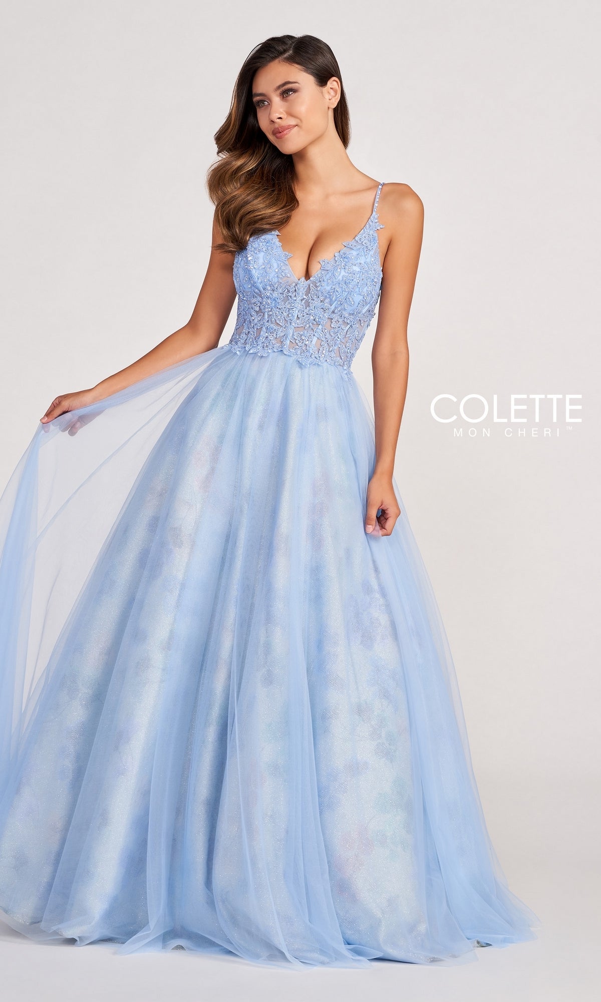 A woman stands against a plain background wearing the Pastel Long Tulle Prom Ball Gown by Colette, featuring a light blue lace bodice and sheer tulle skirt—an elegant choice for prom.