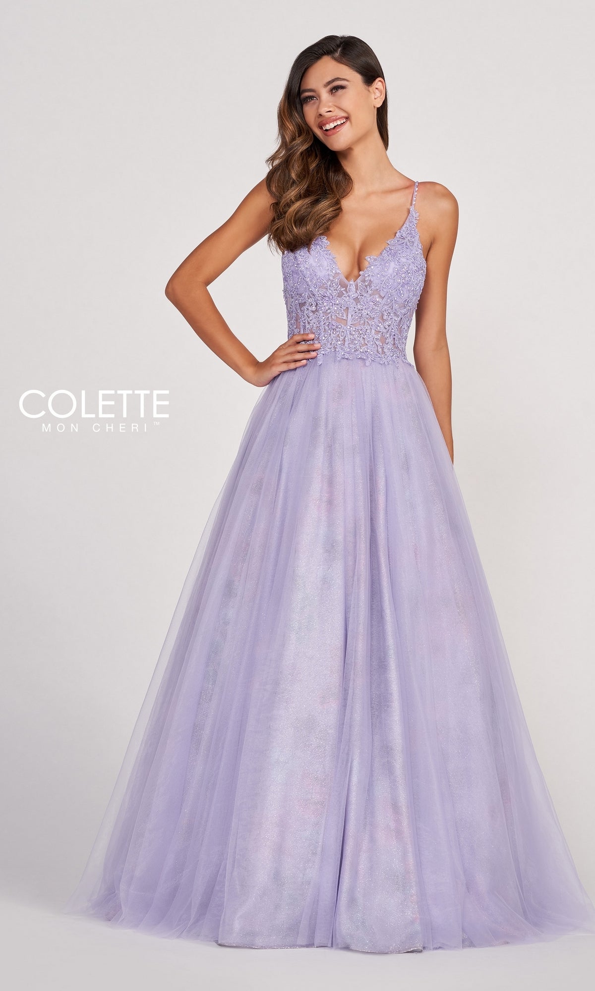A woman wears the Pastel Long Tulle Prom Ball Gown by Colette, featuring a lavender hue, lace bodice, and thin straps, standing against a simple light background.