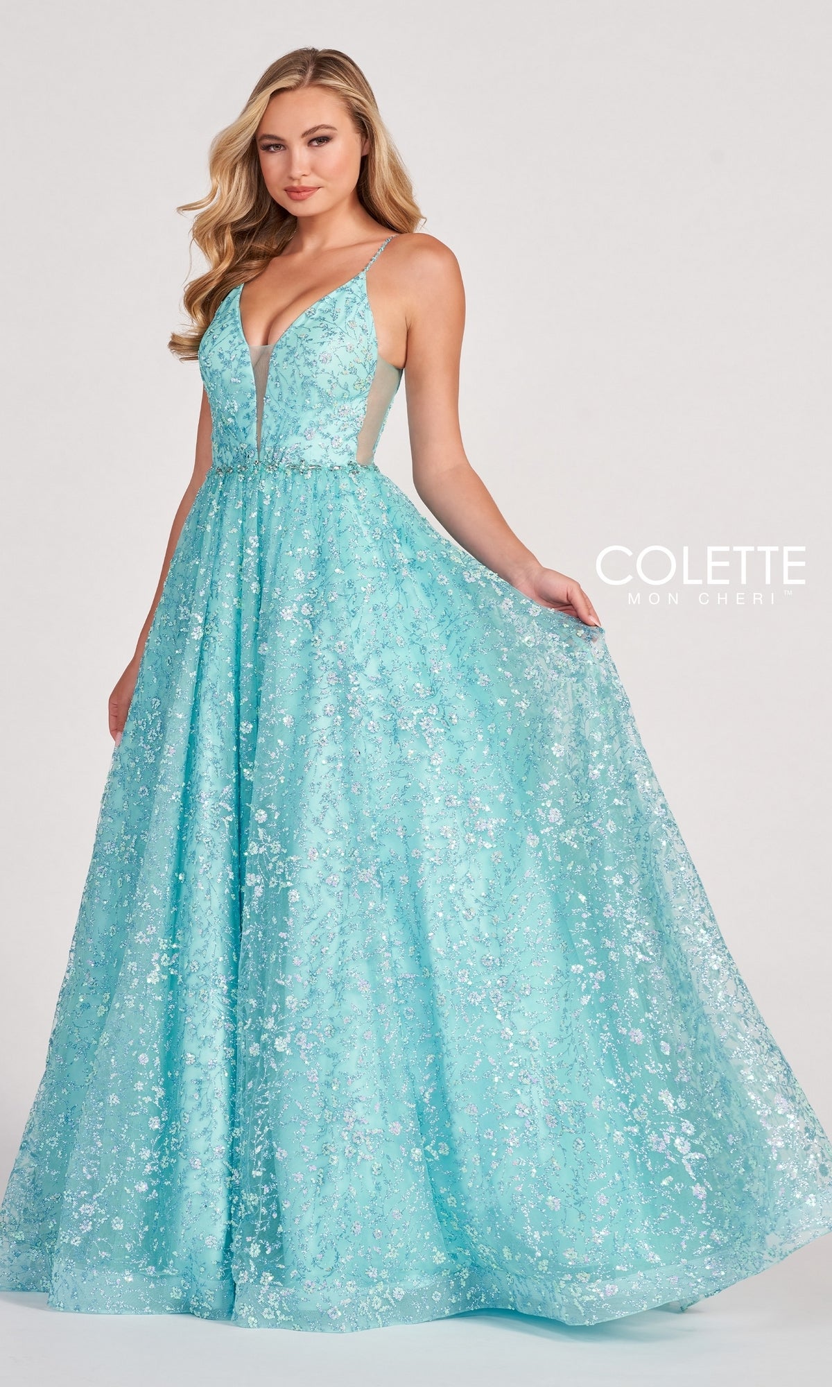 A woman stands against a plain light background, wearing the Backless Tulle Prom Ball Gown CL2016 with a sleeveless, floor-length silhouette, deep V-neckline, glitter print, and sparkling floral sequin embellishments.