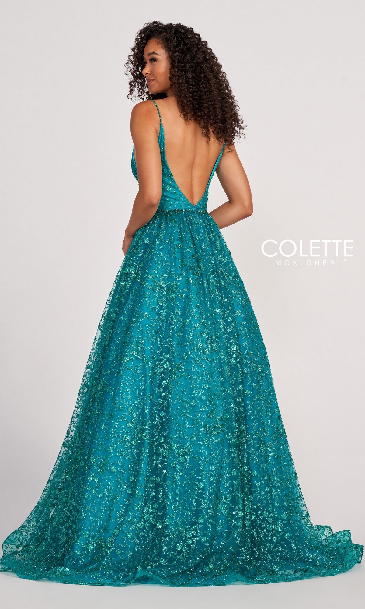 A woman showcases the Backless Tulle Prom Ball Gown CL2016 with glitter print, featuring a teal, floor-length design, deep V-back, and sparkling floral details, standing with her back to the camera.