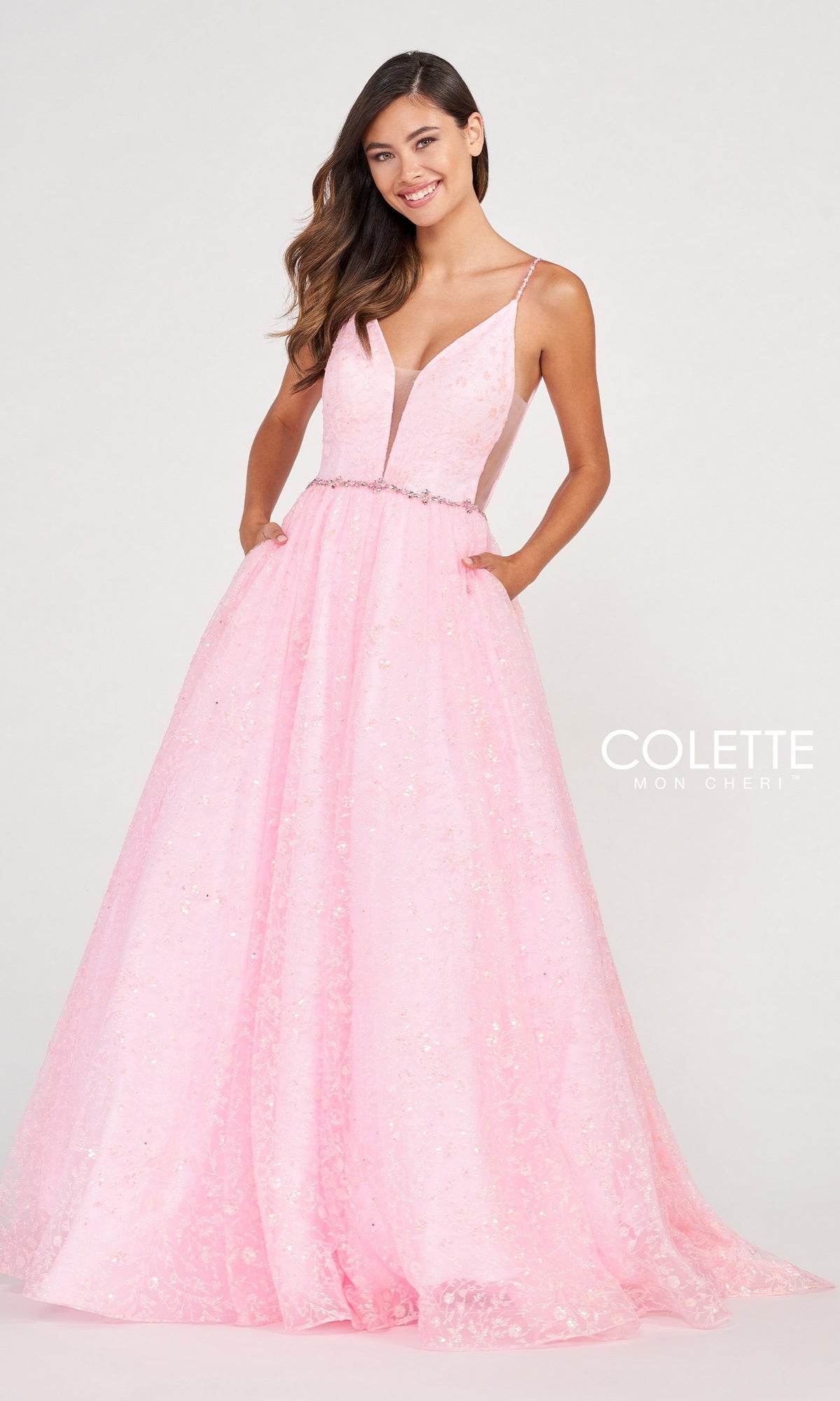 A young woman wears the Backless Tulle Prom Ball Gown CL2016, a light pink, sleeveless, floor-length dress with glitter print, deep V neckline, thin straps, sequin details, pockets, and a fitted waist.