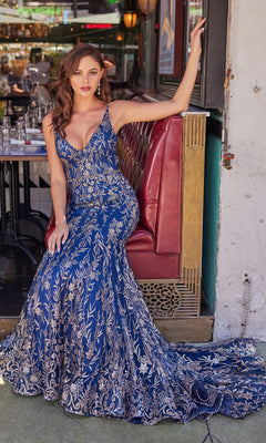Wearing the Colette CL2021 Long Mermaid Glitter Prom Dress in blue and gold, a woman sits elegantly on a red restaurant booth, one arm gracefully resting on the back.