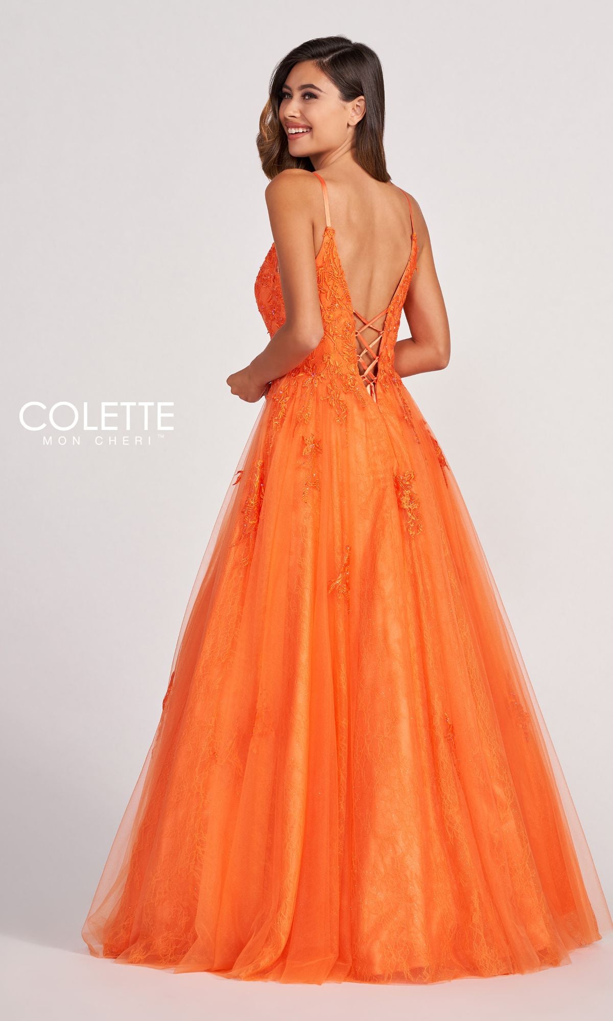 A woman in the Beaded Lace Long A-Line Prom Dress Colette CL2025, featuring orange beaded lace and thin straps, stands facing away and smiles over her shoulder against a plain background.