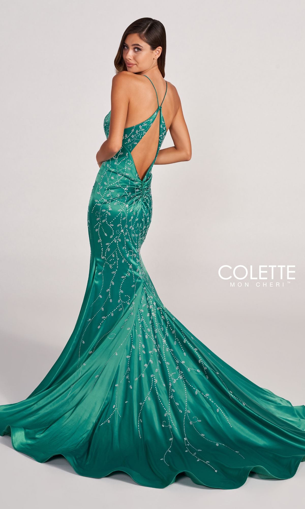 A woman poses against a plain background in the Colette CL2043 Keyhole-Back Long Satin Prom Dress—an emerald green, floor-length gown with thin crisscross straps, a low back, slight train, and stunning shimmering detail.