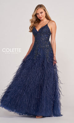 A woman poses gracefully in the Colette CL2044 Feather Prom Ball Gown, a navy blue v-neck evening dress featuring beaded embellishments and feathered details, against a plain background.