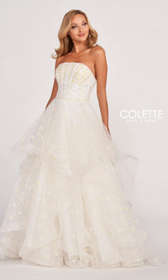 A woman stands against a plain light background, wearing the Colette CL2055 Strapless Daisy Ball Gown featuring a layered tulle skirt and gold floral accents, radiating elegance and timeless charm.
