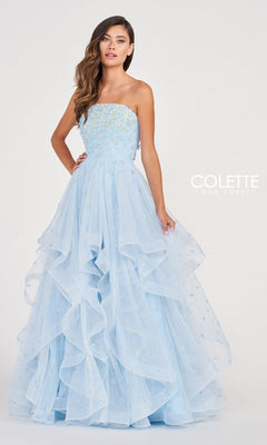 A woman stands against a plain white background wearing the Colette CL2055 Strapless Daisy Ball Gown—a light blue, ruffled-layered dress with bead embellishments.