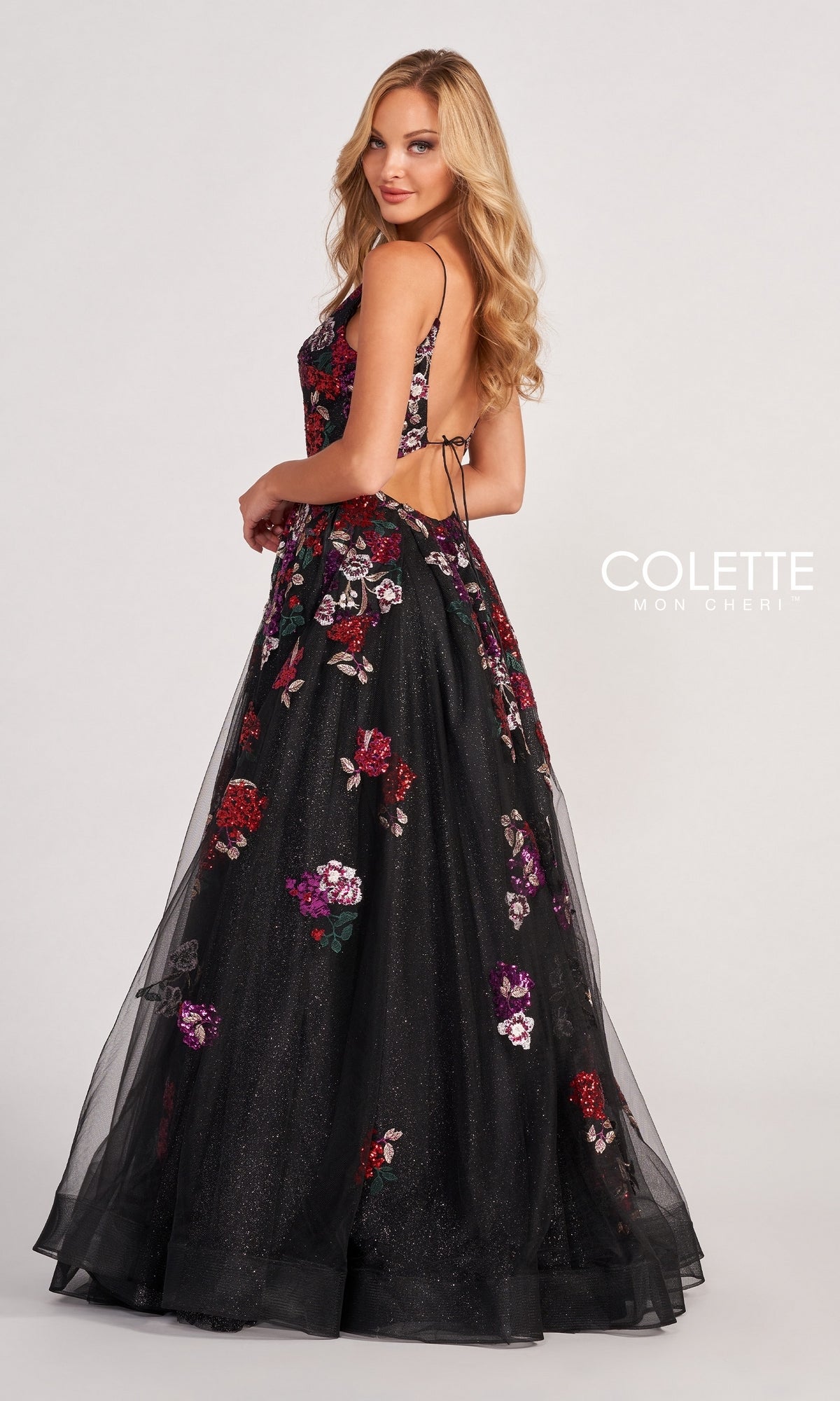 Woman in the Black Prom Dress CL2069 featuring multicolor floral appliques and an open back, standing sideways and looking over her shoulder.