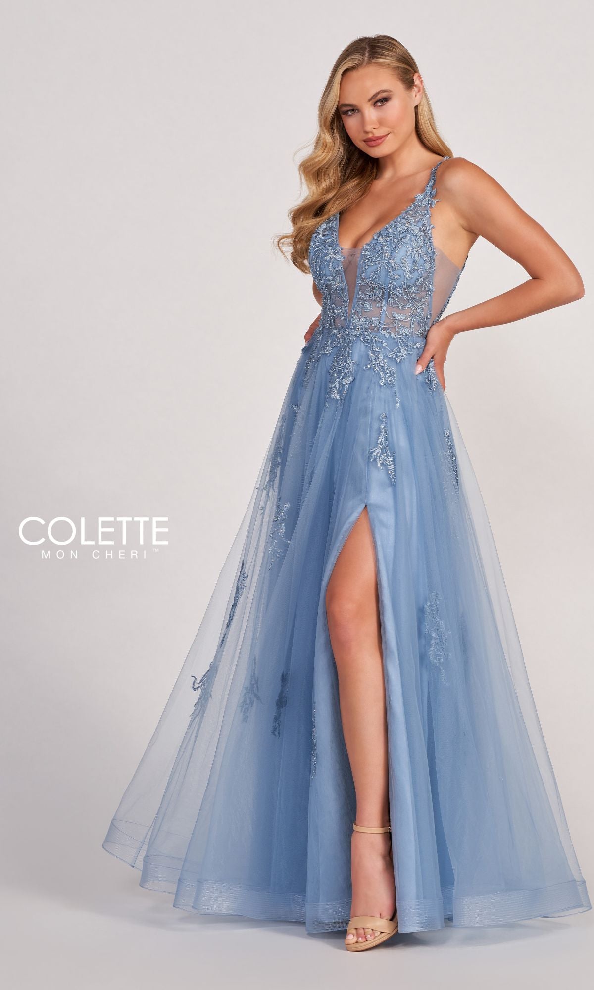 A woman poses in the CL2074 Tulle A-Line Prom Dress, featuring a light blue hue, sleeveless design, floral embroidery, lace appliques, sheer bodice, deep V-neckline, and a high slit against a plain background.
