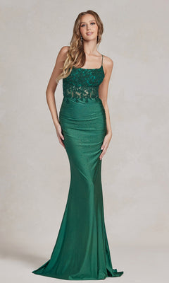 A woman stands wearing a fitted, floor-length green Backless Prom Dress with beaded floral appliques, thin straps, and a lace bodice.