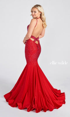 A woman in a Strappy-Back Long Beaded Ellie Wilde Formal Gown with a fitted mermaid silhouette and open back stands facing backward, looking over her shoulder. The floor-length formal dress features subtle sparkles.