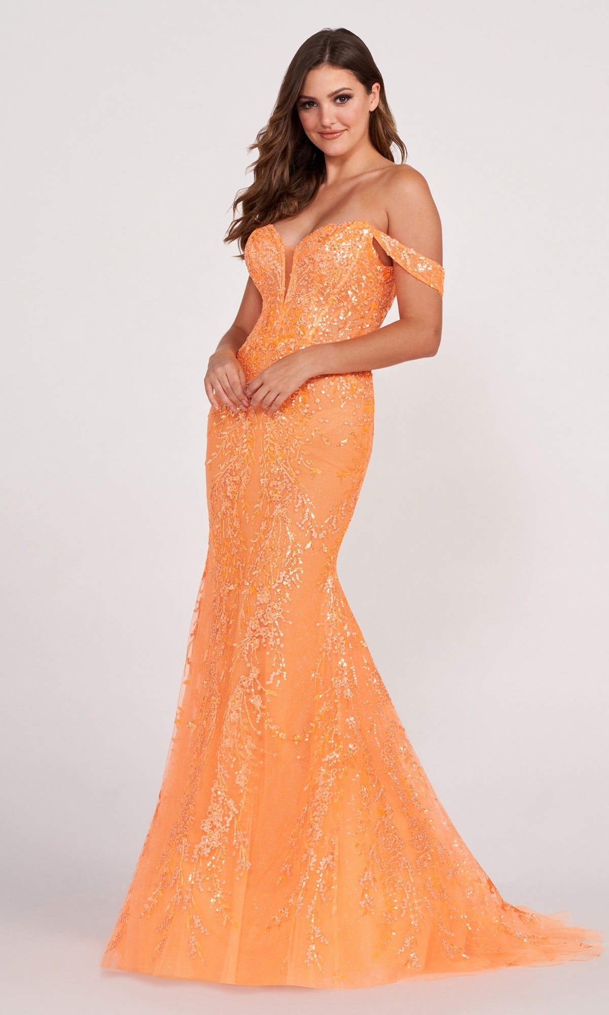 A woman in a lace-embroidered off-shoulder long mermaid gown stands against a plain light background. This fitted, floor-length dress is perfect for making a bold statement at any event.