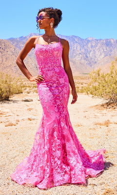 A woman stands in a desert landscape wearing the Ellie Wilde Embroidered-Lace Mermaid Prom Dress, featuring a fitted, floor-length silhouette with floral embroidery and spaghetti straps. Mountains and a blue sky appear in the background.
