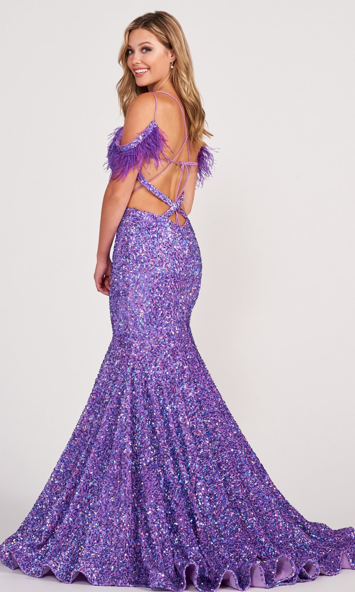 A woman poses, smiling over her shoulder, in the Long Sequin Cut-Out Prom Dress with Feathers—a sparkling purple mermaid gown featuring an open back, crisscross straps, and feathered off-the-shoulder sleeves.