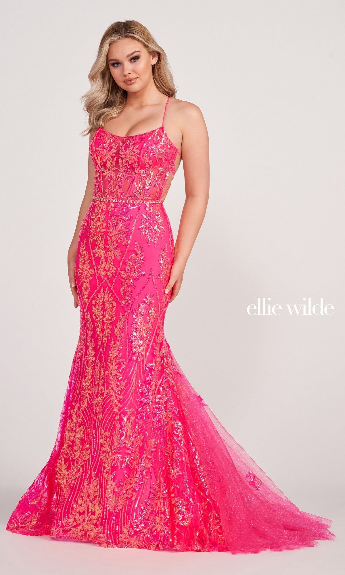 A woman wears the Sheer-Corset Long Sequin Mermaid Prom Dress, a fitted bright pink gown with gold detailing, thin straps, and a flared hem. 