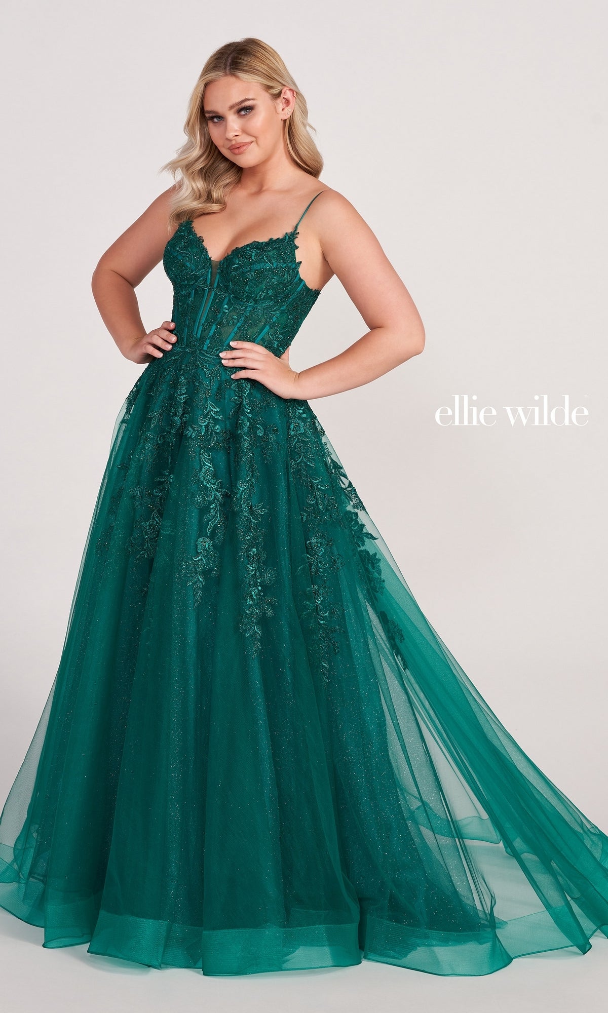 A woman poses with hands on hips in the Sheer-Corset Long Lace Prom Ball Gown EW34036, a floor-length emerald green dress with lace, spaghetti straps, and tulle. The text 