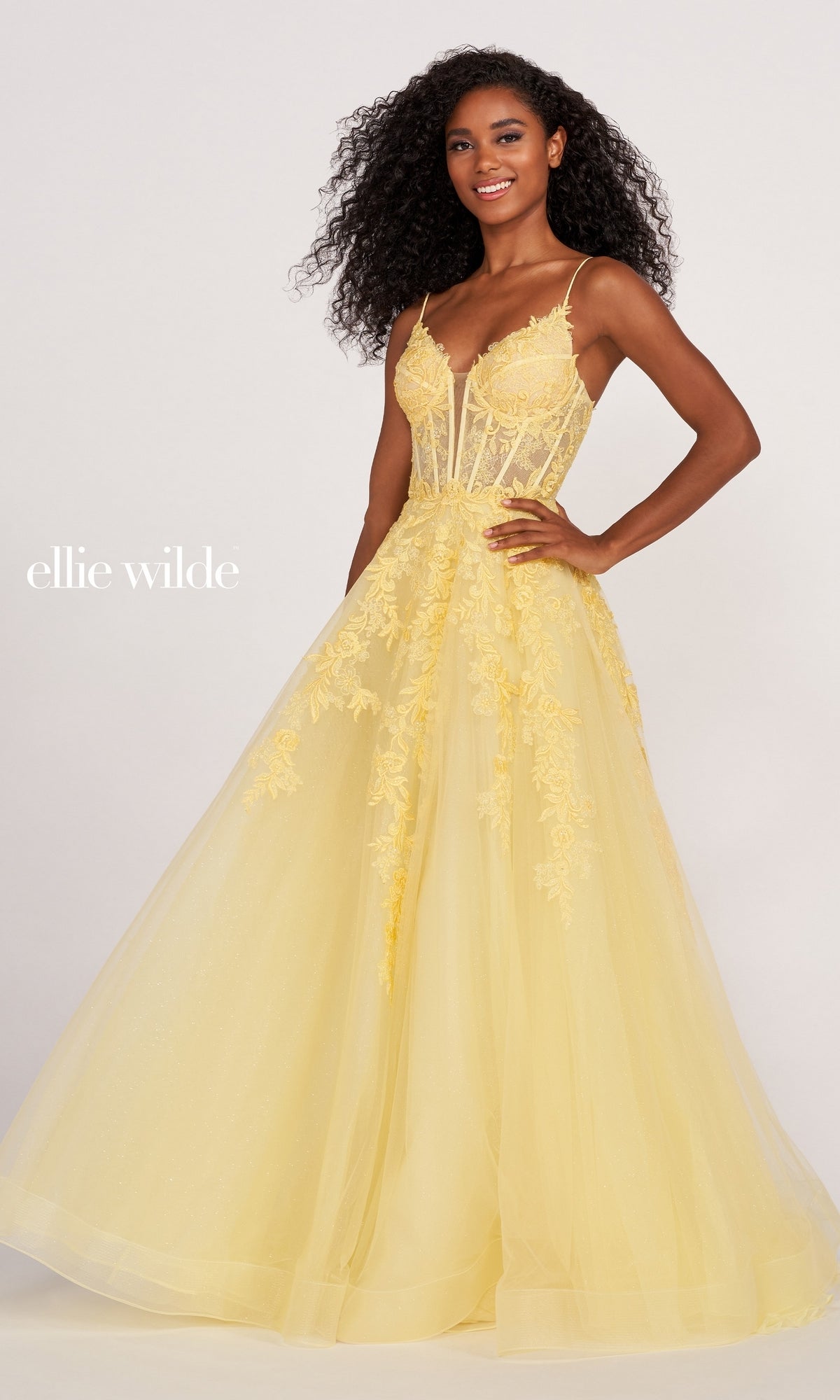 A woman stands against a plain background wearing the Sheer-Corset Long Lace Prom Ball Gown EW34036, a yellow, floor-length lace dress with floral details and a fitted sheer bodice. The text 