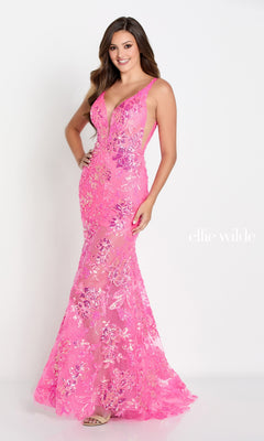 A woman poses and smiles against a white background wearing the Ellie Wilde Sheer-Skirt Long Prom Dress EW34040, a fitted floor-length pink mermaid gown embellished with sequin flowers.