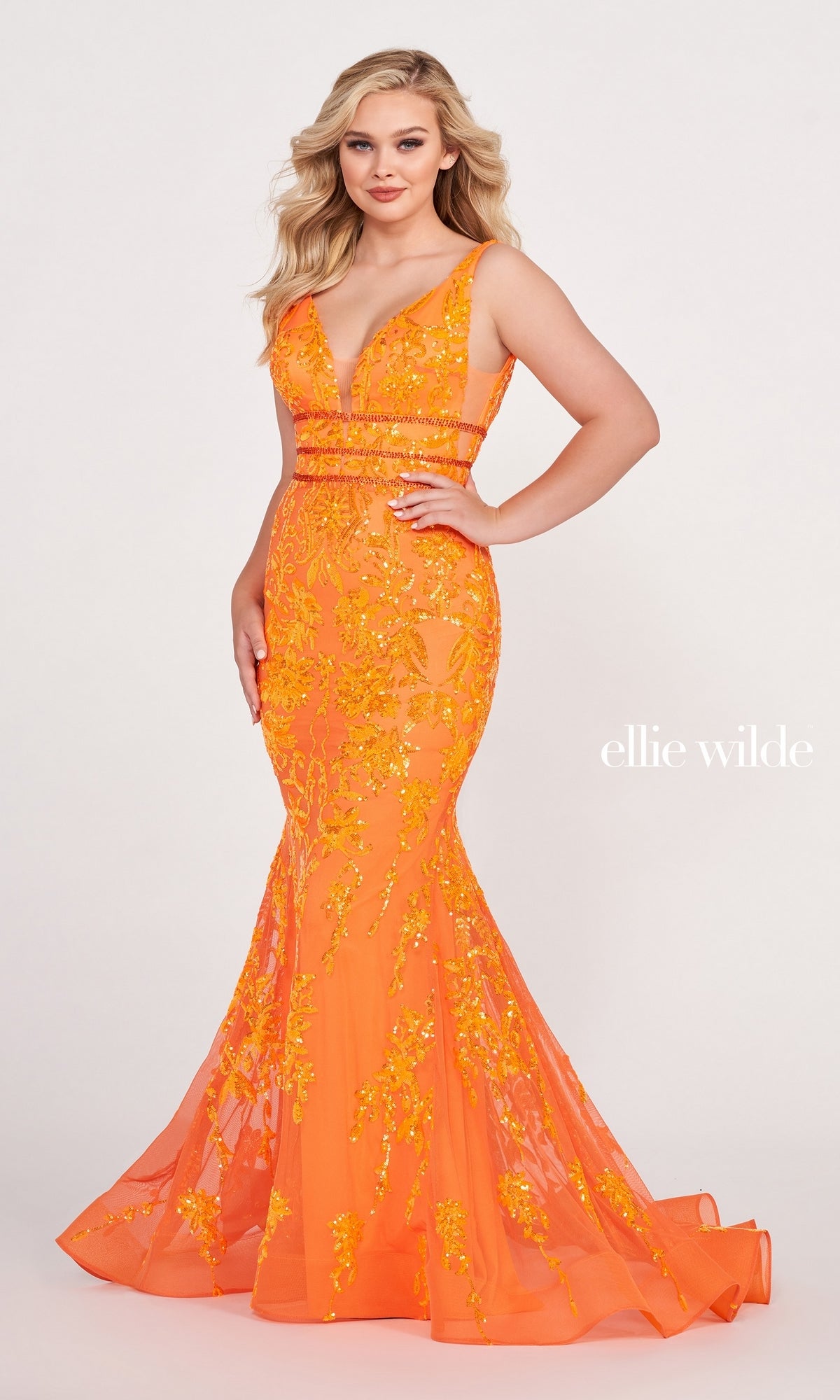 A woman poses against a light background wearing the Banded-Waist Long Sequin Mermaid Prom Dress with floral sequins and deep V neckline. The text 