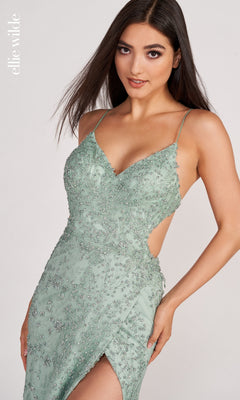 A woman poses against a plain background wearing the Ellie Wilde Backless Long Glitter Prom Dress, featuring light green fabric, beaded details, a high slit, thin straps, and an open back.