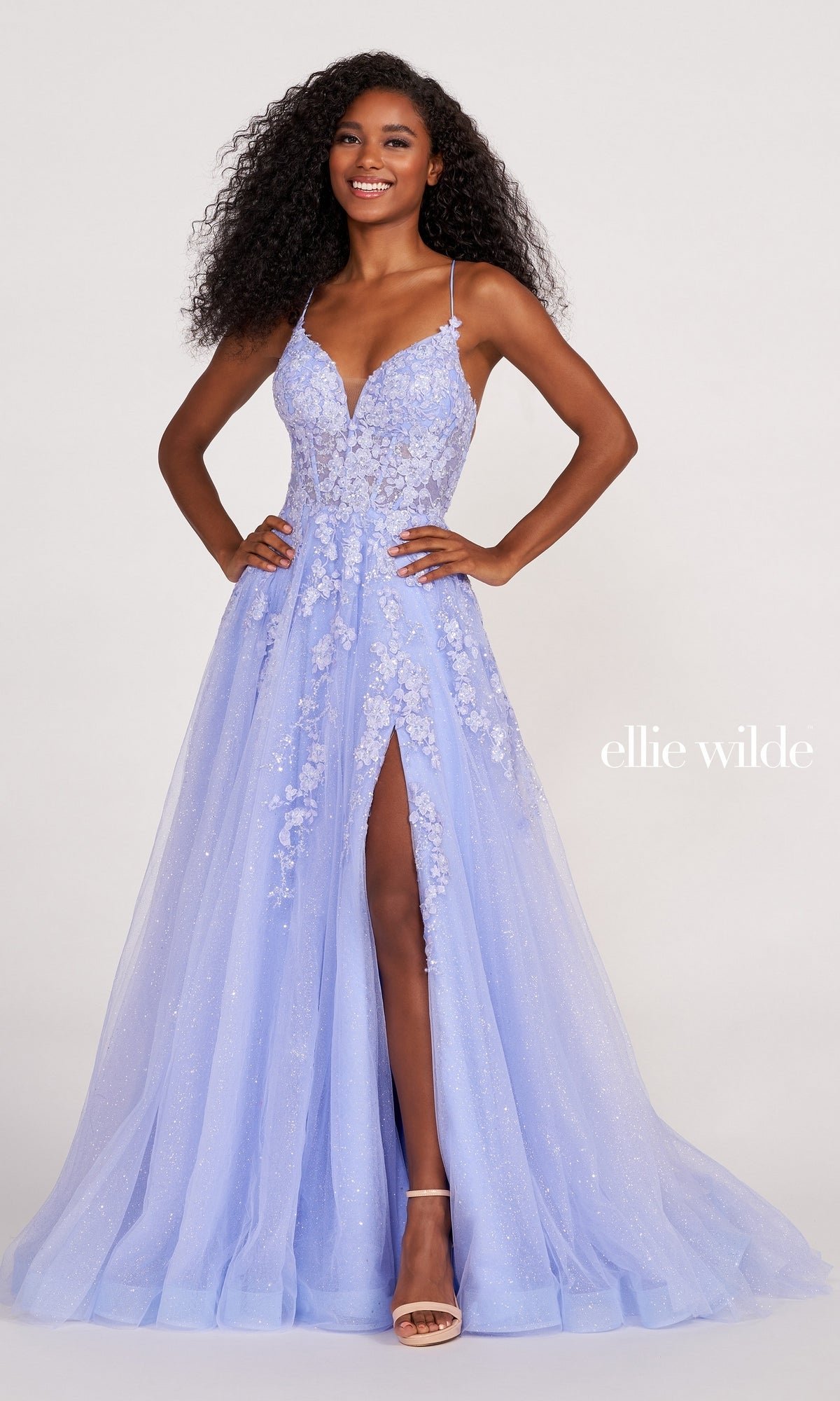 A woman poses in the Ellie Wilde Backless Designer Prom Dress EW34053—a light purple, floor-length gown with floral appliqué, spaghetti straps, a thigh-high slit, and elegant backless design.