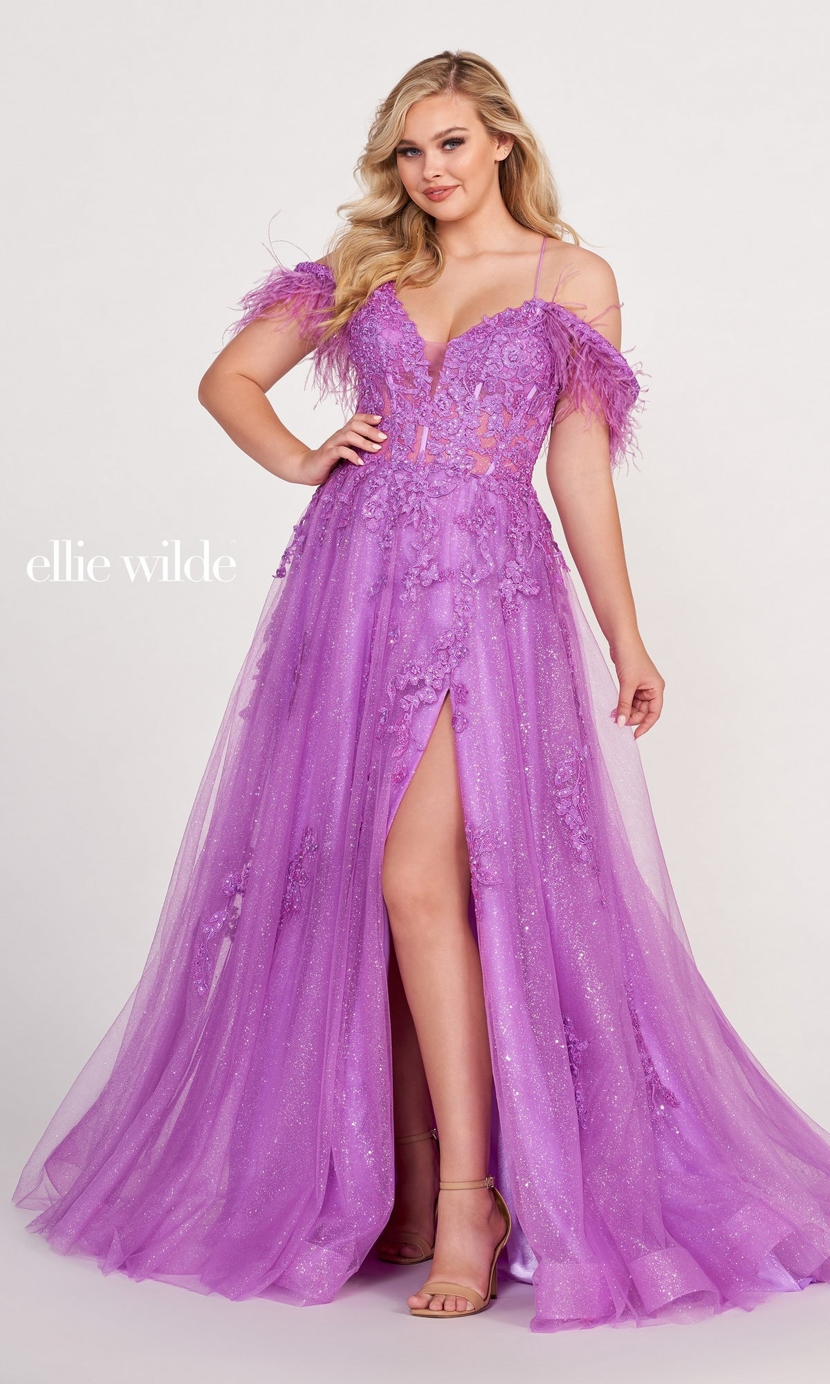 A woman stands against a plain background wearing the Glitter Ball Gown With Off The Shoulder Feather Sleeves, featuring a lavender hue, floral embellishments, feather sleeves, and a high slit.