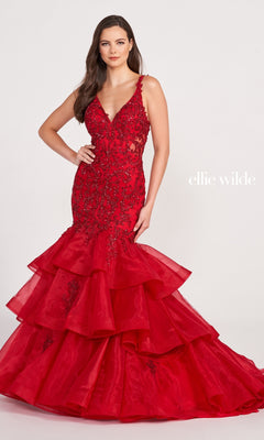 A woman poses in the Layered Skirt Mermaid Ellie Wilde Gown EW34082, a red dress with lace, bead detailing, and a dramatic ruffled hem, against a plain white background. "ellie wilde" appears beside her.