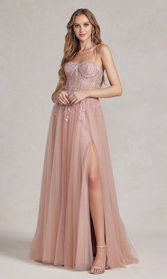 A woman in the Corset-Bodice Long Pastel Prom Dress, featuring blush pink fabric, an A-line silhouette, a sheer lace corset bodice, thin straps, and a high slit, stands against a neutral background.