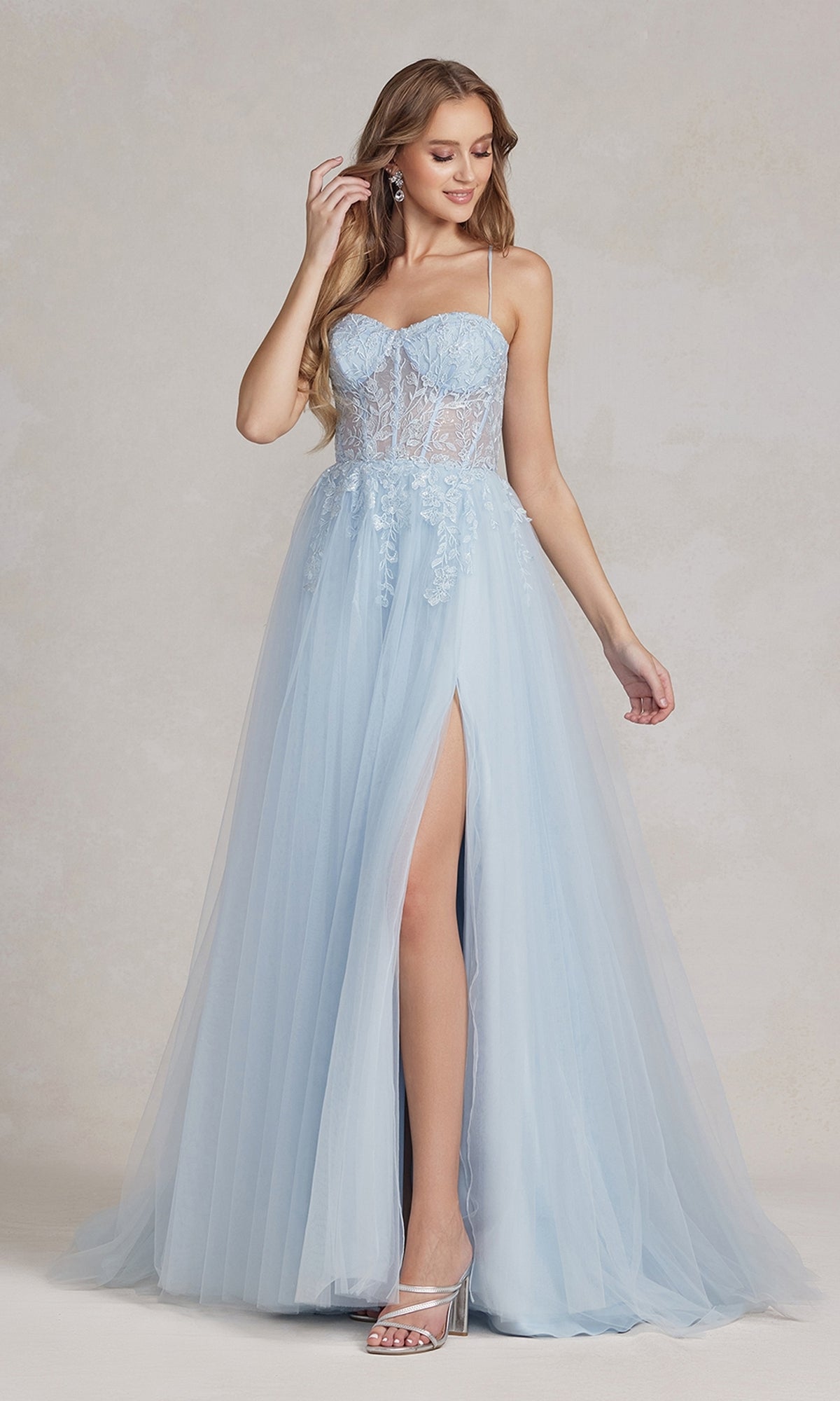 A woman in a Corset-Bodice Long Pastel Prom Dress featuring a sheer lace bodice, spaghetti straps, high slit, and silver heels poses against a neutral background.