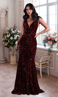 A woman in a PromGirl Deep V-Neck Red Long Sequin Prom Dress stands indoors by a window decorated with floral arrangements and classic decor.