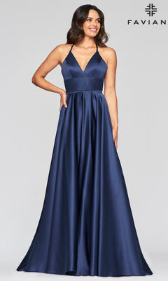 A woman models the Corset-Back A-Line Long Satin Prom Dress by Faviana in navy blue satin with a deep V-neck and thin straps, standing before a plain light background. The Faviana logo appears in the upper right corner.