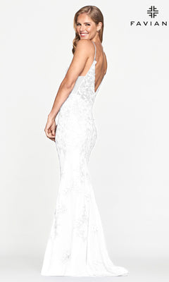 Woman in a fitted white Sheer-Sides Long Lace Prom Dress by Faviana, featuring a deep V-back, stands sideways and smiles. The "FAVIANA" brand name appears in the top right, showcasing this elegant designer gown.
