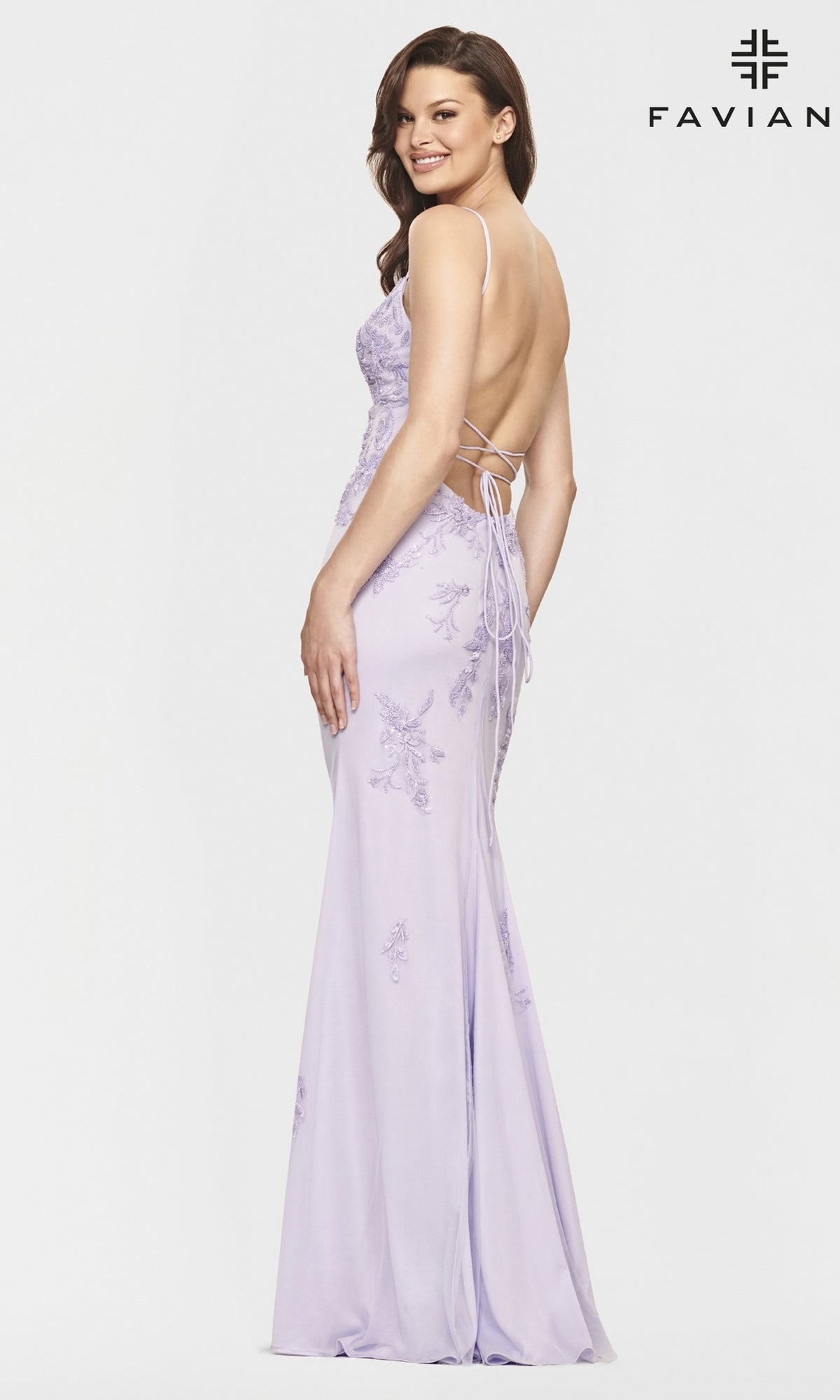 A woman poses in the Strappy-Back Long Light Pink Prom Dress by Faviana, featuring lace-up details, subtle floral embroidery, and a fitted, floor-length silhouette.