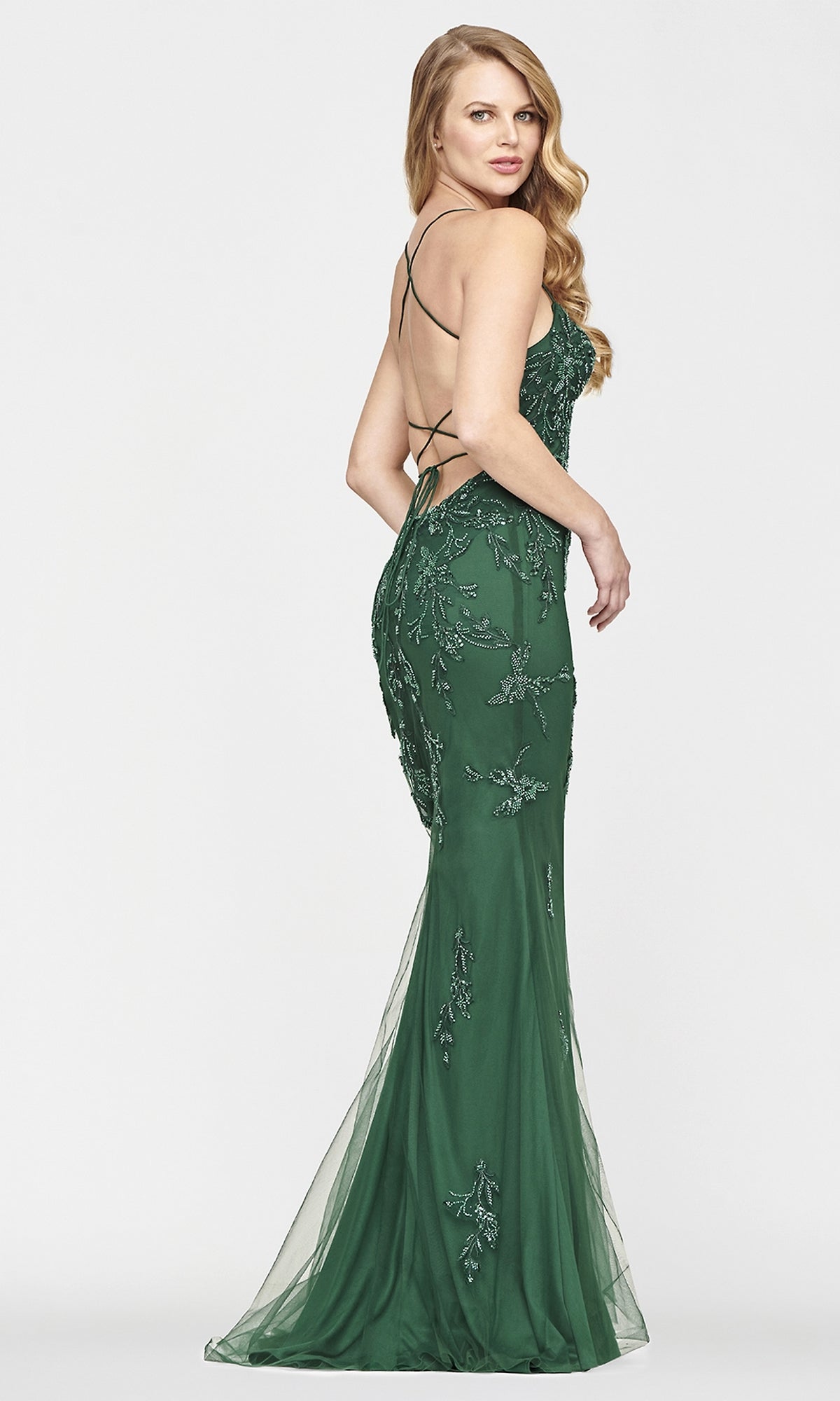 A woman poses in profile against a plain white background, wearing a fitted, floor-length Faviana strappy open-back long yellow prom dress.