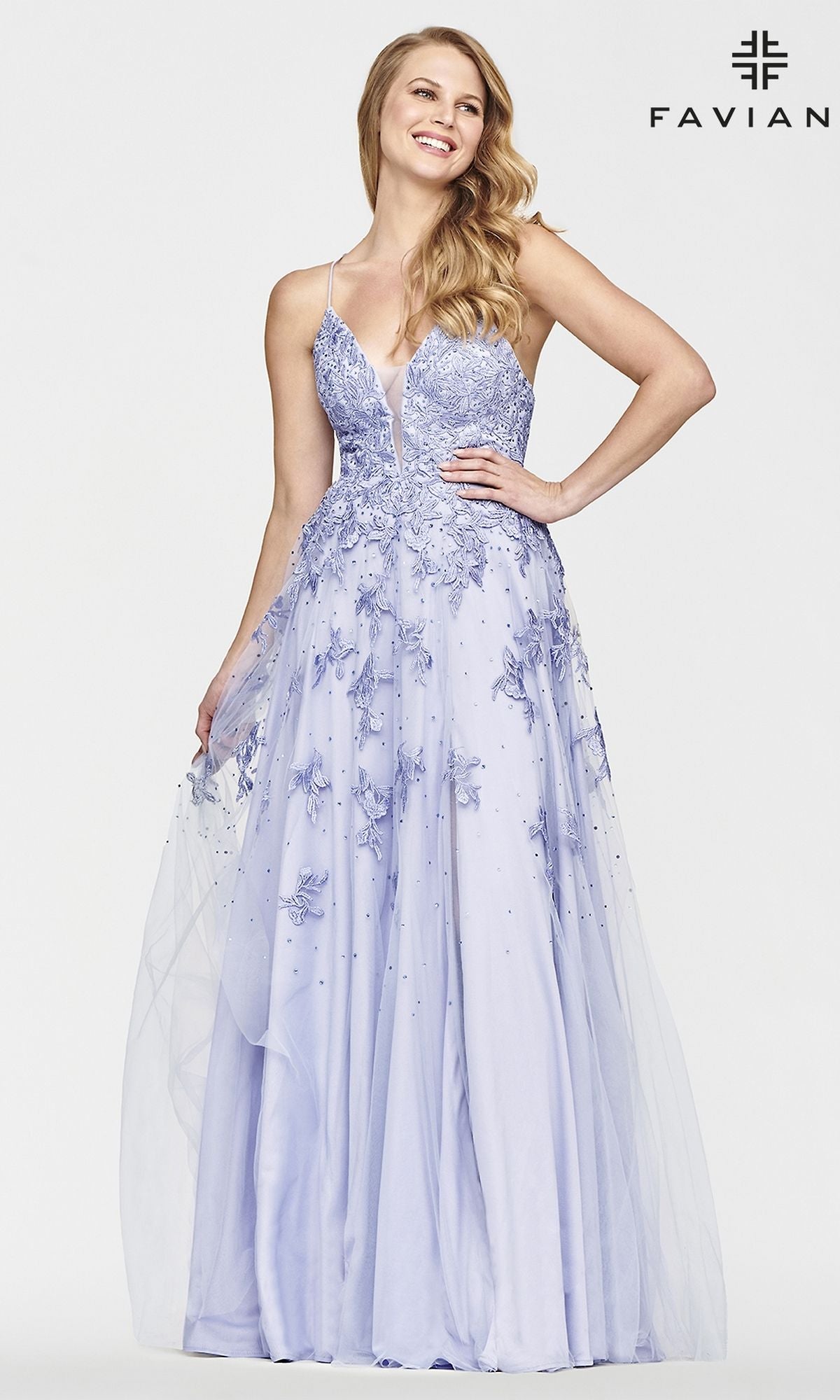 A woman smiles with one hand on her hip, wearing the Faviana Embroidered A-Line Long Prom Dress in lavender. The gown has 3-D embroidered flowers, a sheer overlay, thin straps, and a deep V neckline.