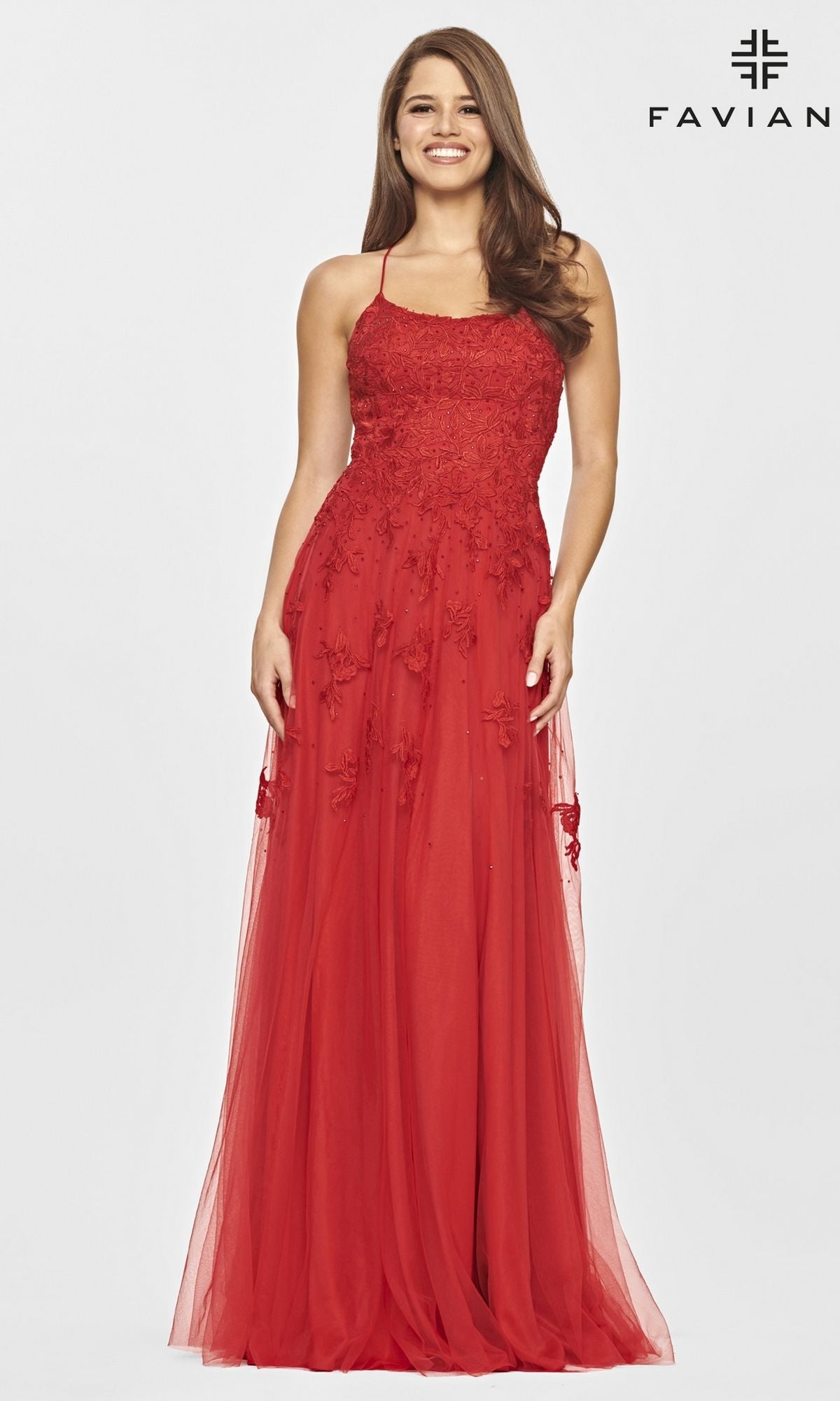 A woman stands and smiles against a plain white background, wearing the elegant Faviana Strappy-Back Long Lace A-Line Prom Dress with tulle details. The 