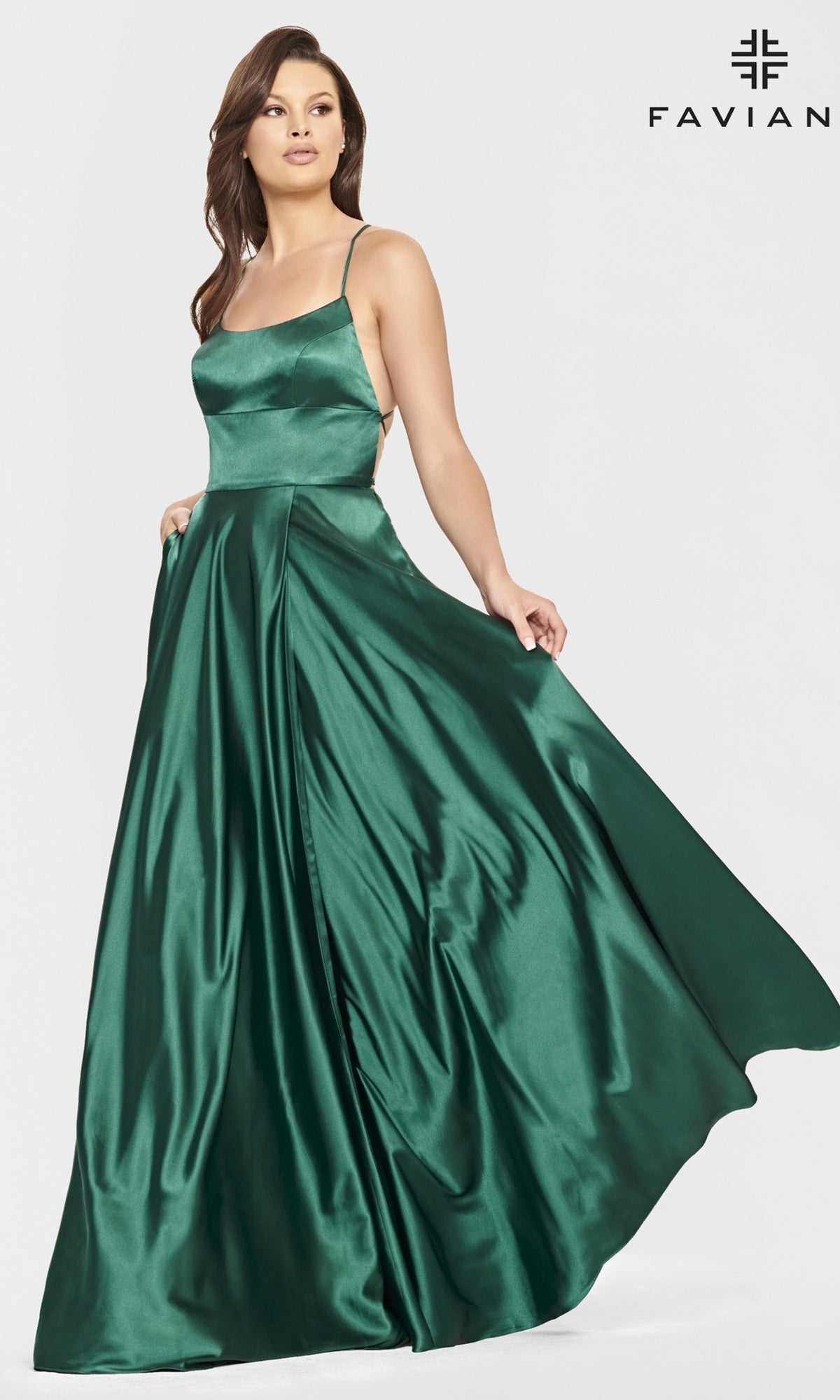 A woman models the Long Open-Back Formal Prom Dress by Faviana—an emerald green, sleeveless satin gown—posed against a plain white background with the Faviana logo in the top right corner.