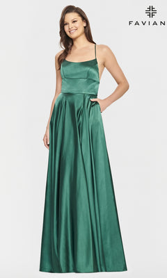 A woman poses against a plain background wearing the Long Open-Back Formal Prom Dress by Faviana—an emerald green, sleeveless satin A-line gown with a square neckline, fitted bodice, full-length skirt, and one hand in her pocket.