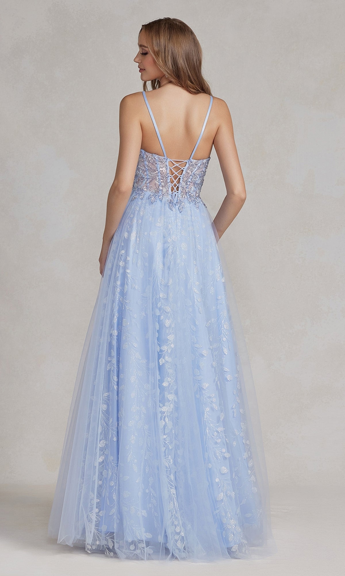 A woman faces away, wearing the Periwinkle Illusion-Bodice Long Prom Dress featuring thin straps, a lace-up back, and delicate floral embroidery.