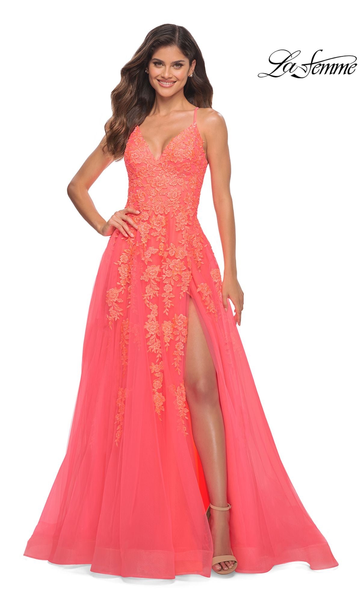 A woman smiles against a plain white background wearing the Hot Coral La Femme Open-Back Long Prom Ball Gown, featuring floral lace appliqué, spaghetti straps, a sweetheart neckline, and a thigh-high slit.