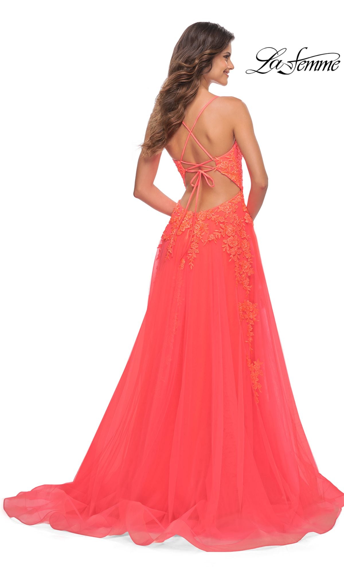 A woman models the Hot Coral La Femme Open-Back Long Prom Ball Gown, featuring lace details, floral embroidery, an open back, and crisscross straps against a white background.