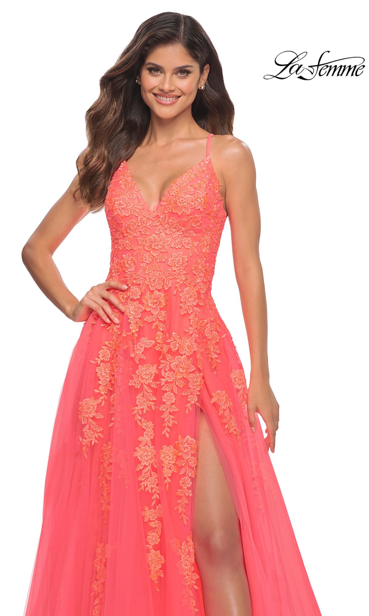 A woman stands smiling in a sleeveless Hot Coral La Femme Open-Back Long Prom Ball Gown with floral embroidery and a thigh-high slit. The La Femme logo appears in the top right corner.