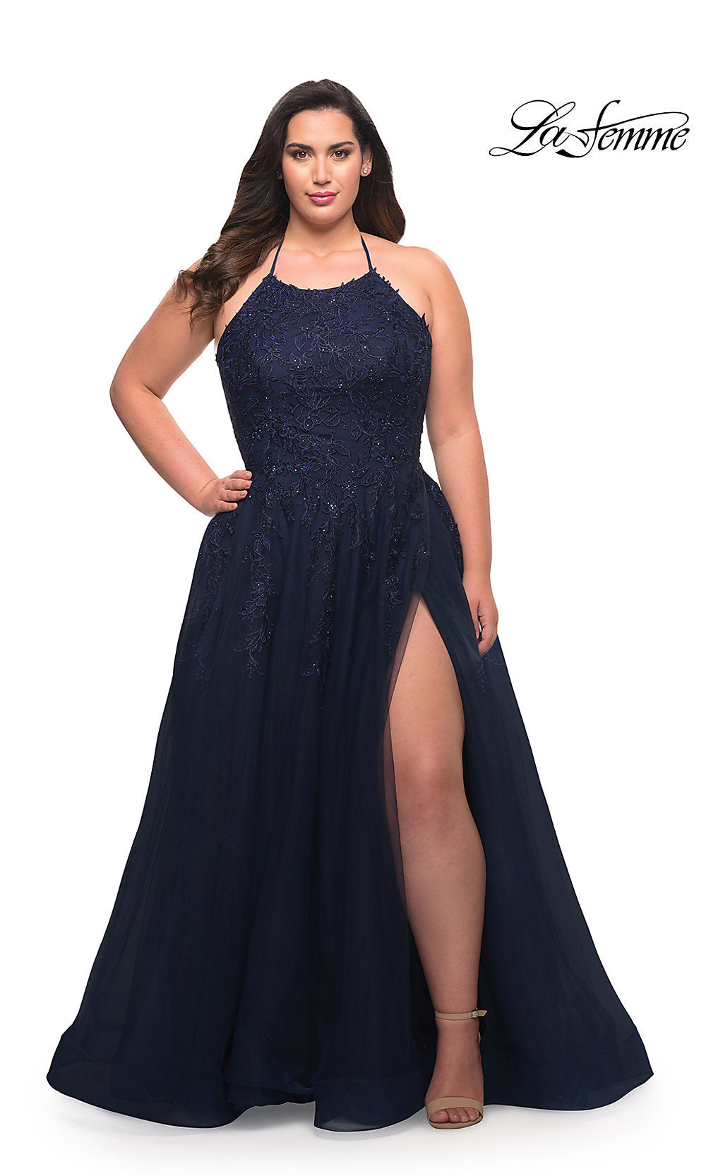 A woman stands confidently with one hand on her hip wearing a navy La Femme Corset-Back Long Plus-Size Prom Dress with lace details and a thigh-high slit. The La Femme logo appears in the top right corner.