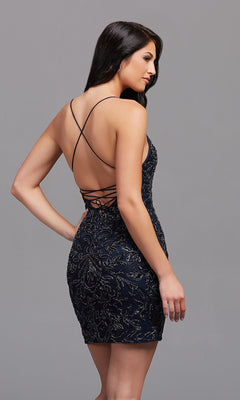 A woman wears the PromGirl Open-Back Tight Sequin Short Prom Dress, a fitted, sleeveless dark blue party dress with beaded designs and crisscross straps over an open back, standing before a gray background.