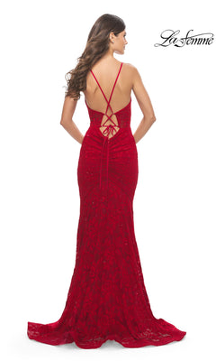 A woman stands facing away, wearing the La Femme Long Lace Prom Dress with a fitted, floor-length red design, strappy back detail, and floral lace accents.