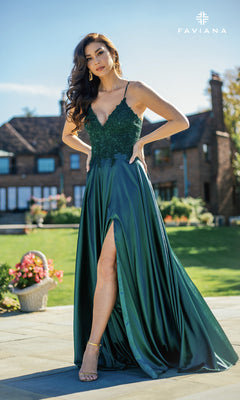 Woman outdoors on a patio in front of a brick house, wearing the Faviana Lace-Bodice Long A-Line Prom Dress—an elegant dark green, sleeveless gown with a thigh-high slit and delicate embroidered lace.