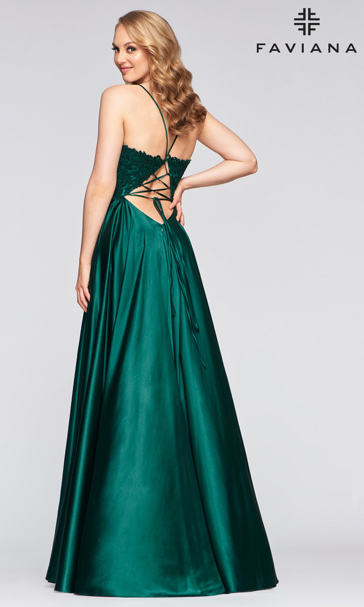 Woman models the Faviana Lace-Bodice Long A-Line Prom Dress in dark green satin featuring a lace-up open back, standing and looking over her shoulder; Faviana logo appears in the top right corner.