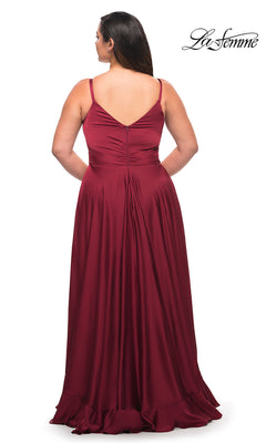 A woman faces away in a sleeveless, floor-length burgundy satin Long Plus-Size La Femme Prom Dress with a V-back and ruffle hem. The La Femme logo is displayed in the top right corner.