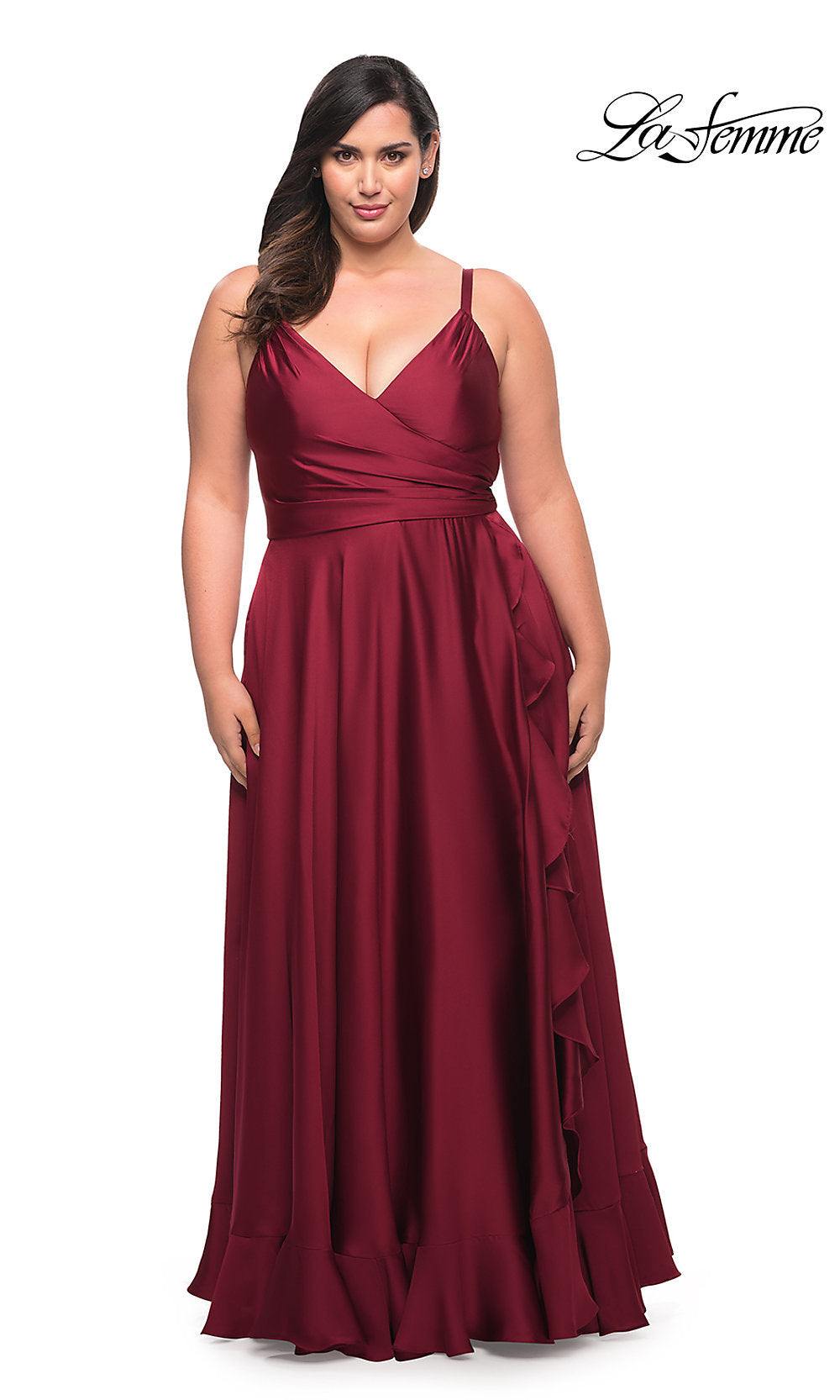 A woman models the Long Plus-Size La Femme Prom Dress, featuring a sleeveless, floor-length burgundy design with a V-neckline and ruffle hem, against a plain white background. The La Femme logo appears in the top right corner.
